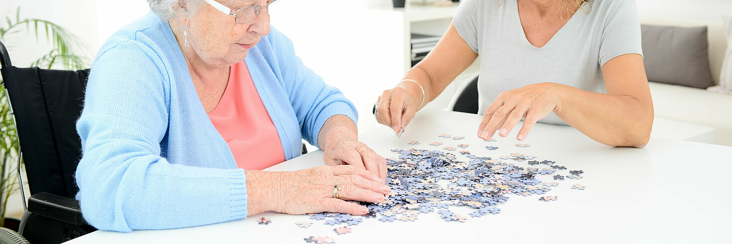 24-Stunden-Betreuerin ist mit Kundin über ein Puzzle gebeugt